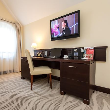 Radisson Blu Hotel, Danzica Esterno foto The photo depicts a corner of a room featuring a stylish desk with a chair and a television mounted on the wall above. The desk has various items on it, possibly including a telephone, clock, and some decorative elements or stationery. There is a lam