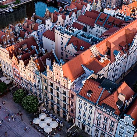 Radisson Blu Hotel, Danzica Esterno foto The photo shows a bird's-eye view of a picturesque urban area, likely in a historical city. It features a cluster of buildings with a mix of architectural styles, characterized by colorful facades and predominantly red rooftops. The buildings seem to