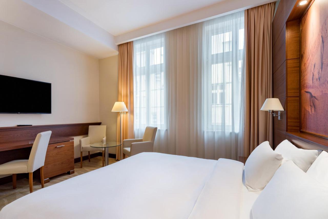Radisson Blu Hotel, Danzica Esterno foto The photo depicts a modern hotel room. It features a neatly made bed with white linens, flanked by two pillows. On the wall opposite the bed, there is a flat-screen television mounted. There are two windows with sheer curtains that allow natural ligh