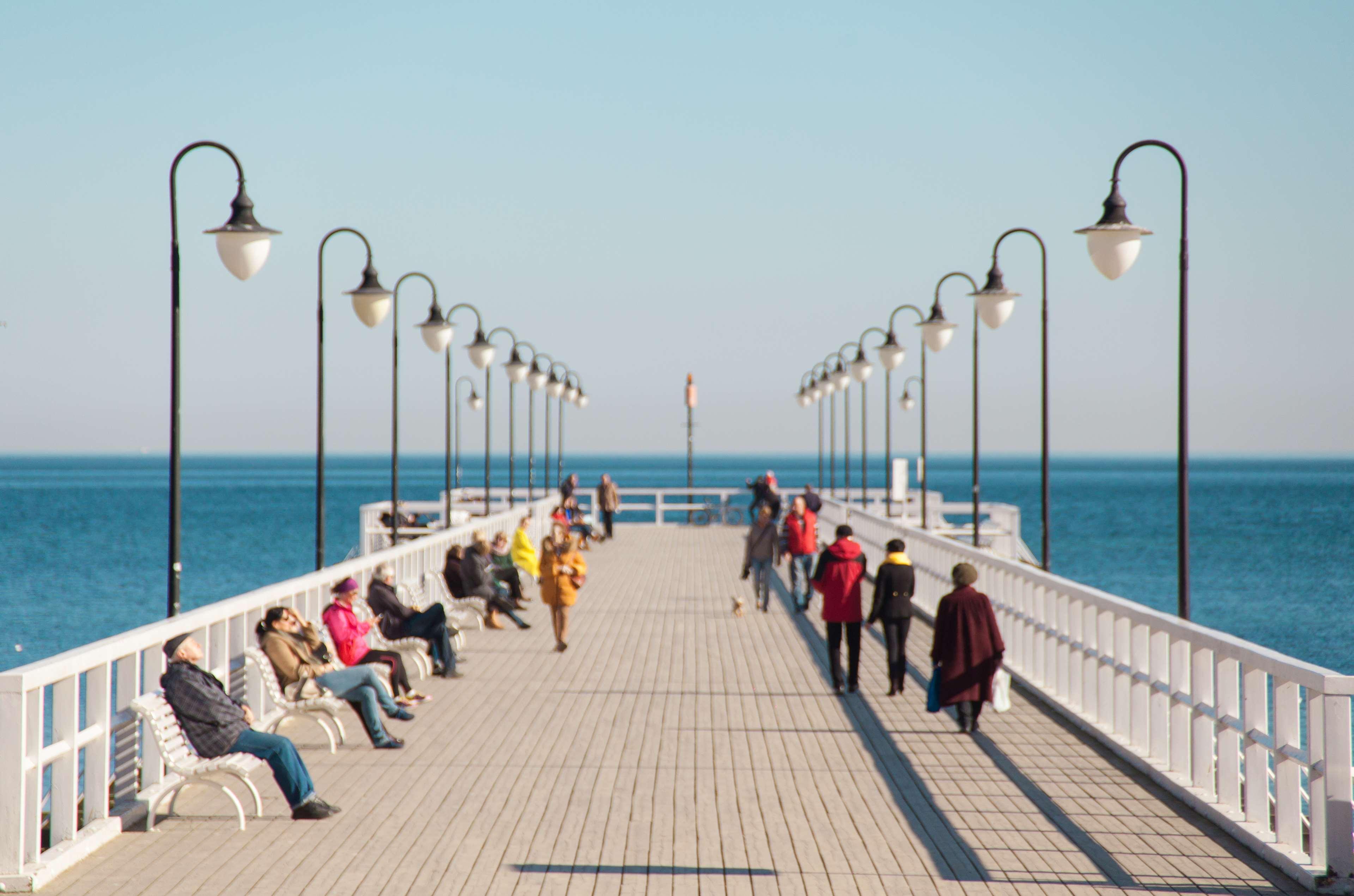 Radisson Blu Hotel, Danzica Esterno foto The photo shows a scenic pier extending out into the water. There are several people enjoying the space, some sitting on benches, while others are walking along the wooden walkway. The pier is lined with decorative street lamps, and the calm sea is v