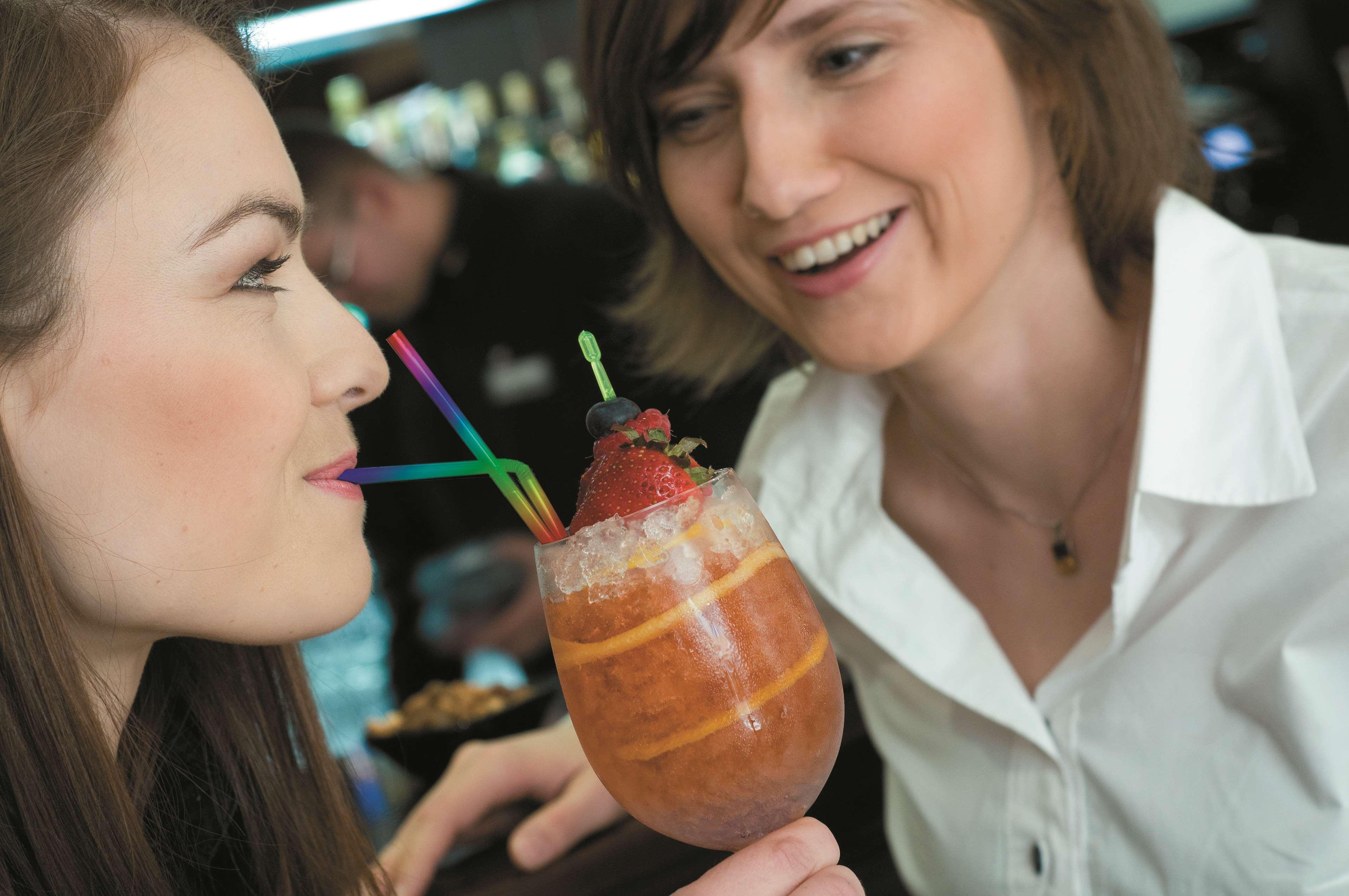 Radisson Blu Hotel, Danzica Esterno foto The photo shows two women engaging with each other, smiling and enjoying a moment together. One woman is holding a colorful drink in a large glass adorned with ice, fruit, and multiple straws. The other woman looks on with a friendly expression, cont