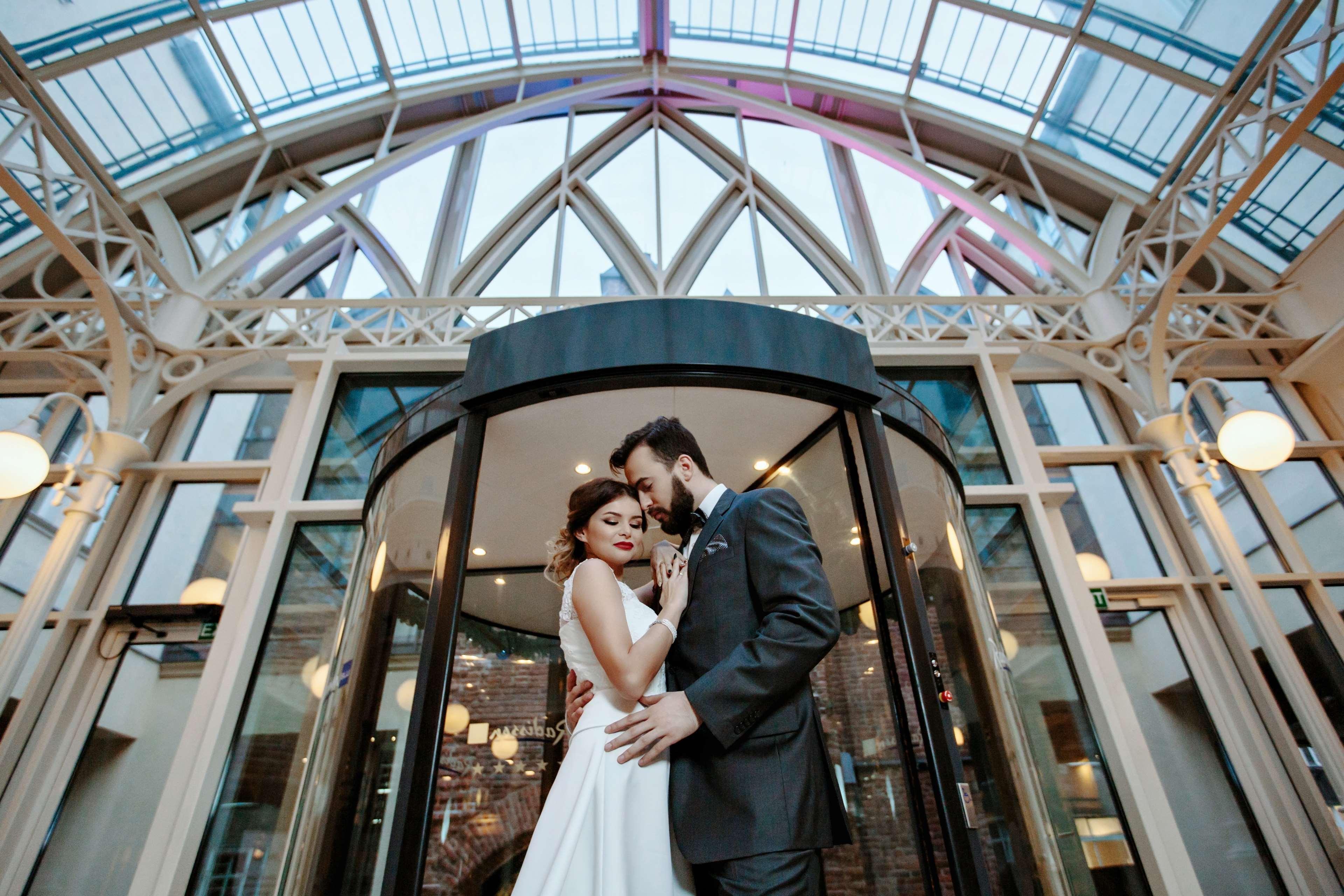 Radisson Blu Hotel, Danzica Esterno foto The photo shows a romantic scene featuring a couple in formal attire, likely celebrating their wedding. They are positioned in front of a round glass door, which is partially open. The couple is standing close together, with their foreheads touching,