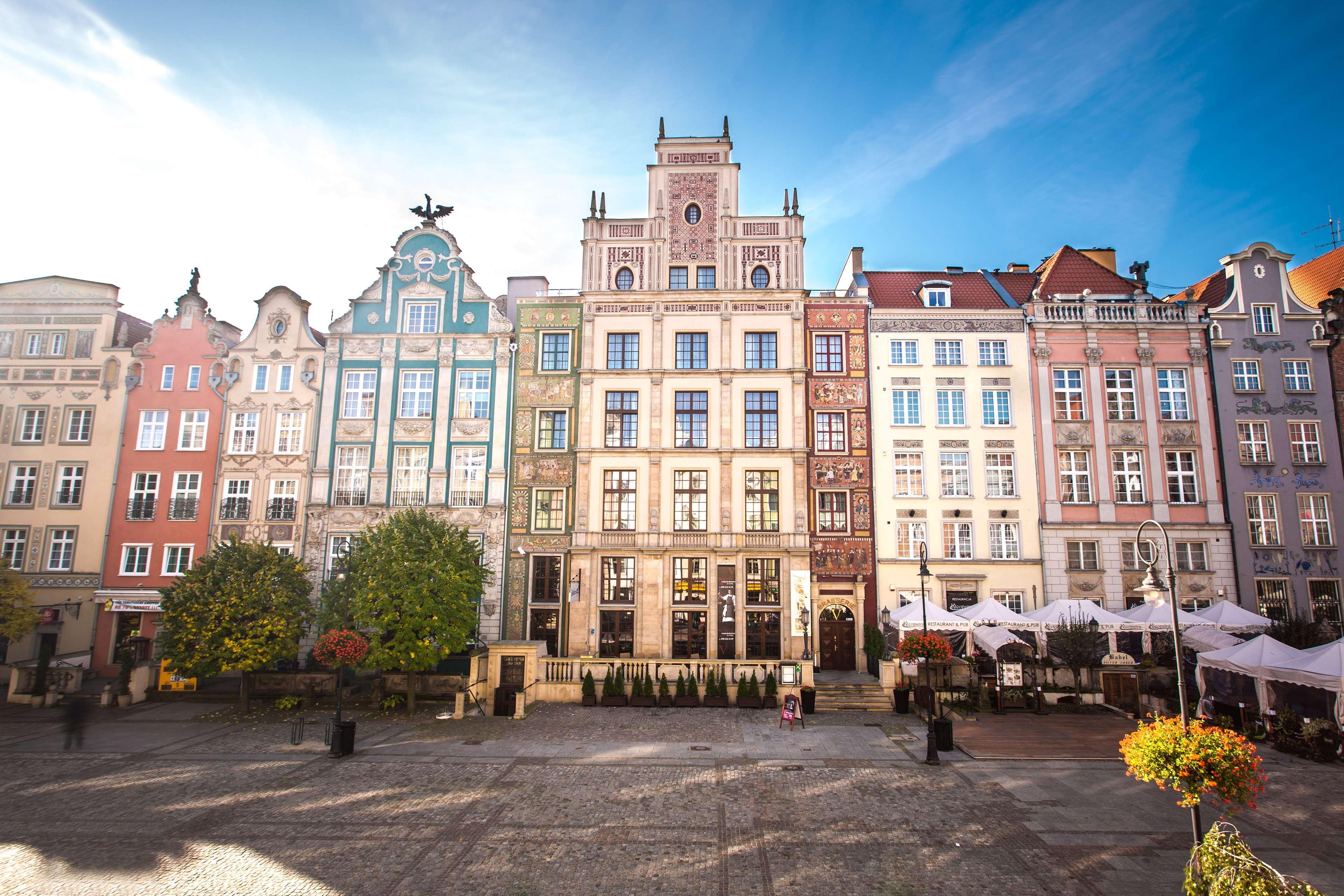 Radisson Blu Hotel, Danzica Esterno foto The photo depicts a picturesque square in a historic European city, likely Gdańsk, Poland. The scene features an array of colorful, well-preserved buildings with ornate architectural details. These buildings are characterized by vibrant facades in va