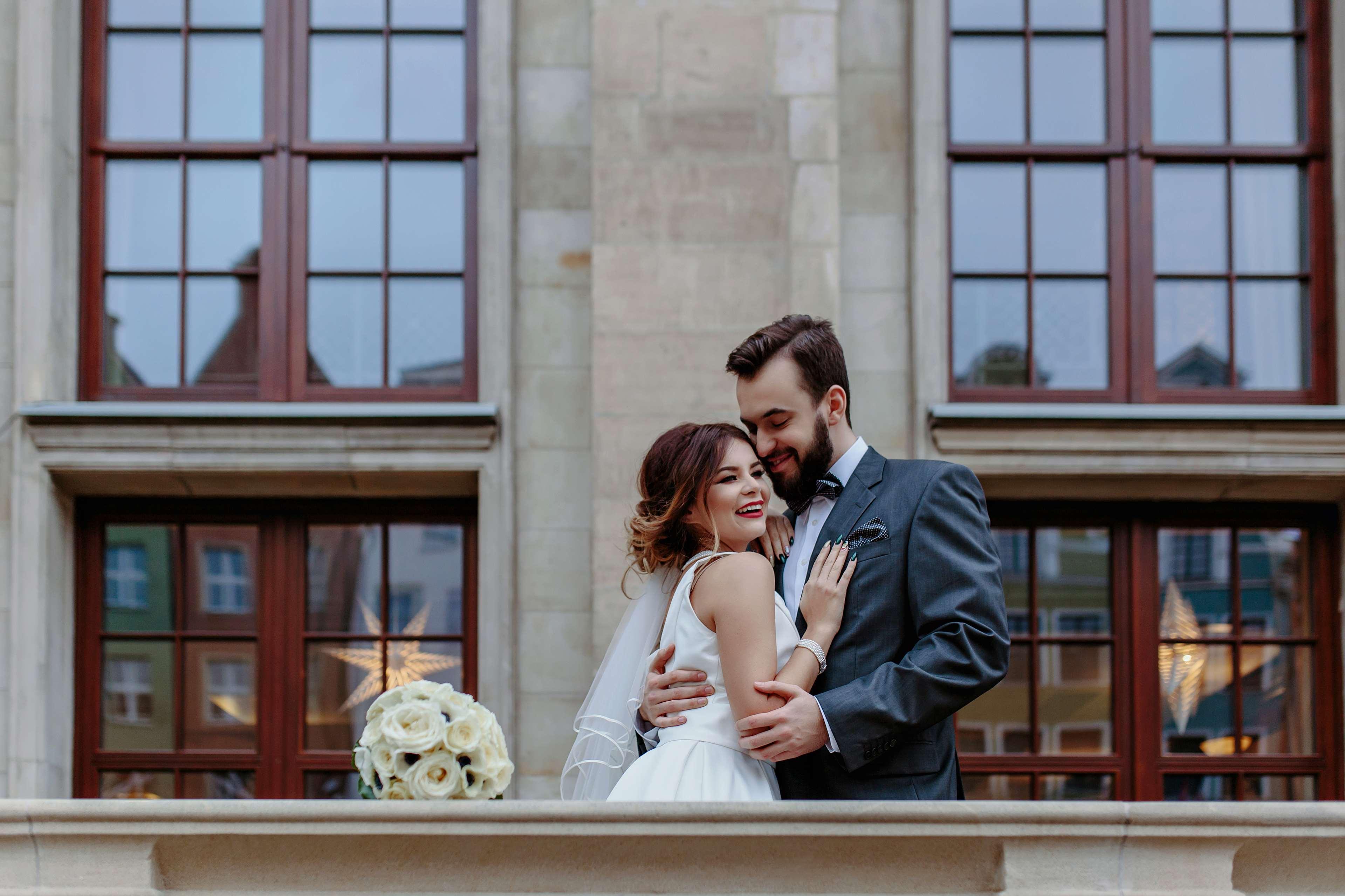 Radisson Blu Hotel, Danzica Esterno foto The photo depicts a joyful couple embracing in a romantic pose. The woman, dressed in a white wedding gown, is smiling and appears to be looking at the man, who is wearing a dark suit. They are standing in front of large windows, which suggest an ele