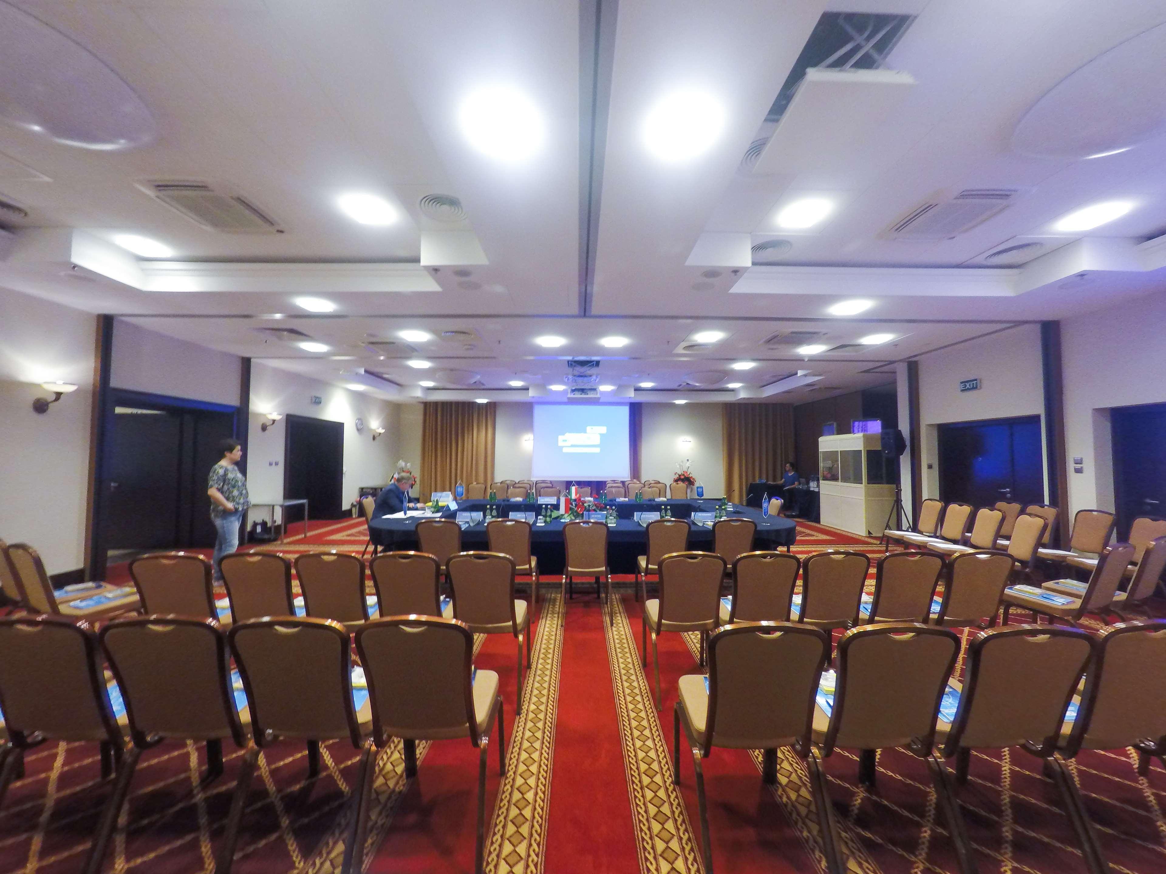 Radisson Blu Hotel, Danzica Esterno foto The photo shows a conference room set up for a meeting or presentation. There are several rows of beige chairs arranged in front of a long table, which is also set up for participants. A large screen or projector is positioned at the front of the roo