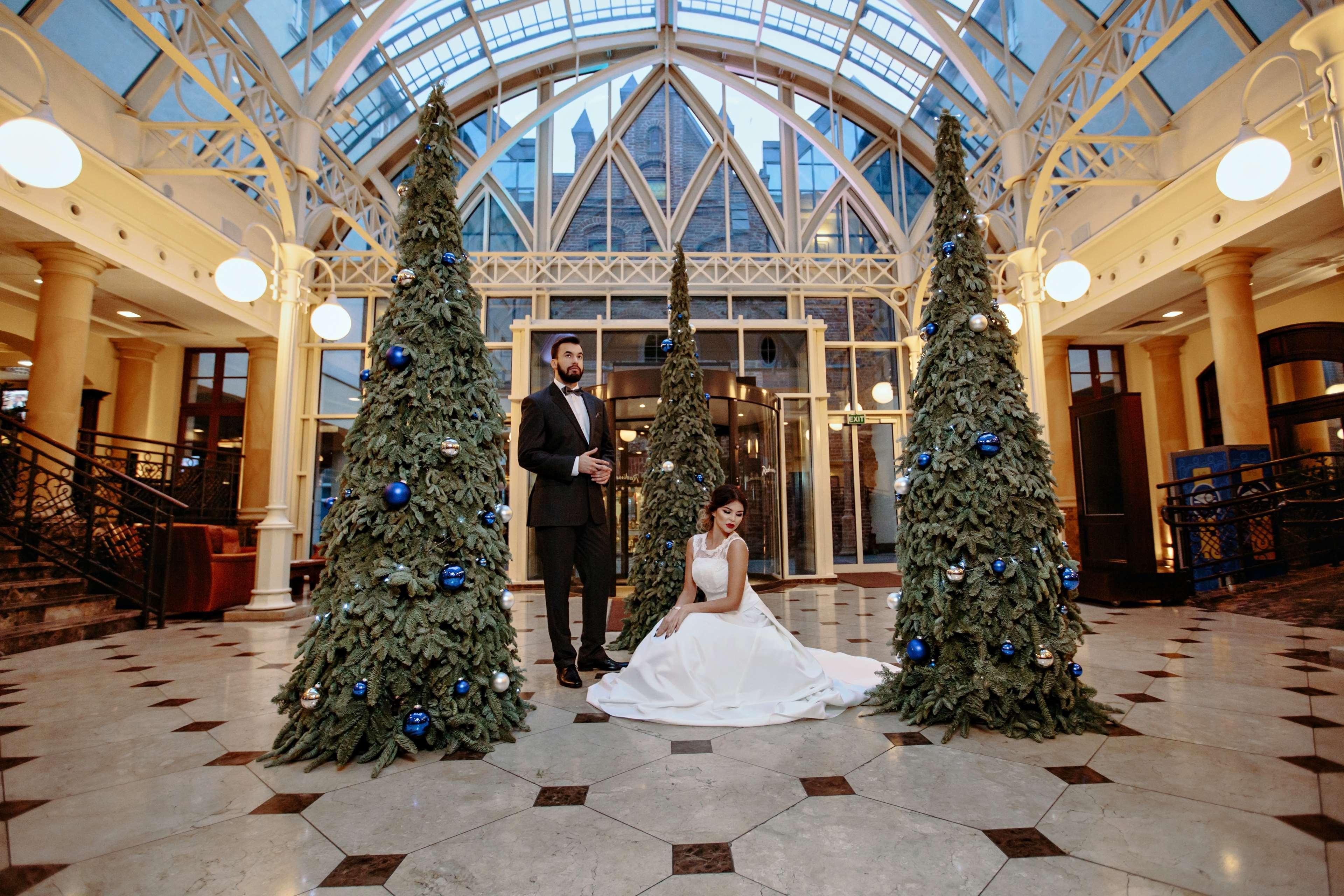 Radisson Blu Hotel, Danzica Esterno foto The photo shows a groom in a tuxedo standing next to a bride in a white wedding dress. They are positioned in a beautifully decorated indoor space, which features large glass windows and elegant architectural details. Surrounding them are three green