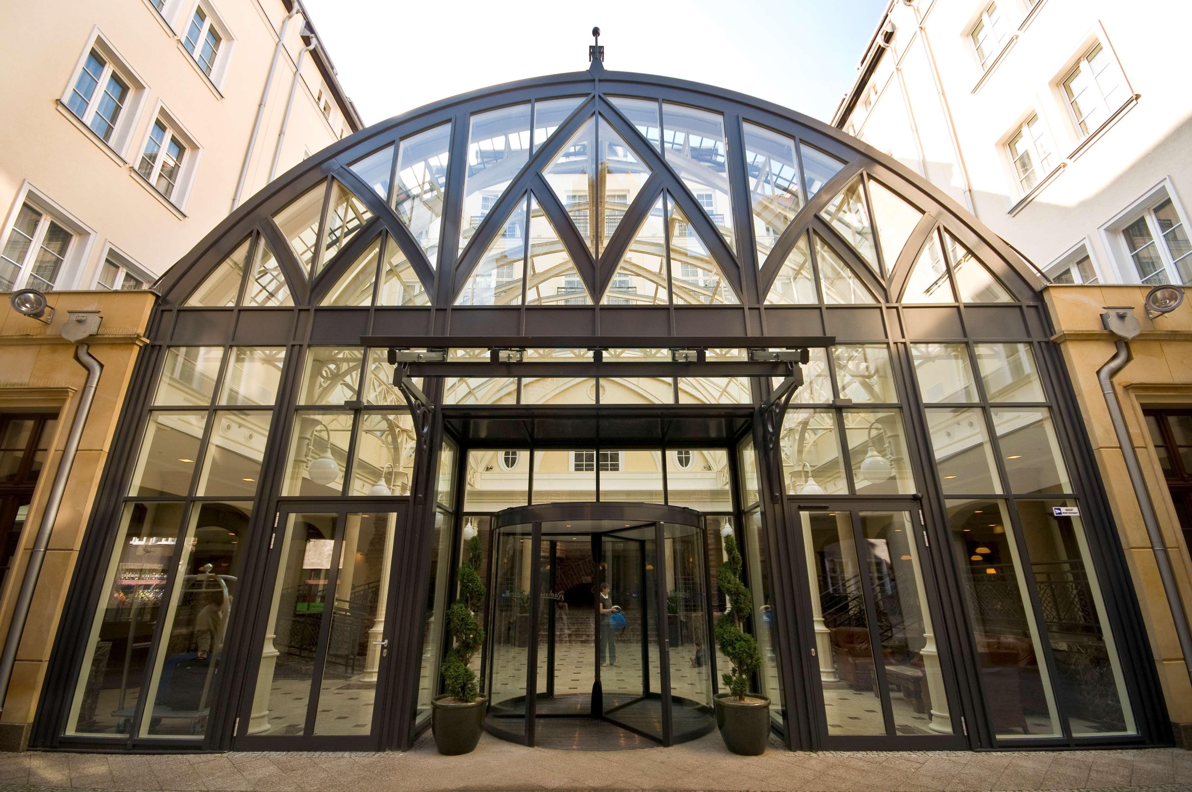 Radisson Blu Hotel, Danzica Esterno foto The photo shows a modern glass entrance, featuring a large, arched roof structure. The facade is predominantly made of glass and metal, allowing natural light to illuminate the interior. There are revolving doors at the center, flanked by symmetrical