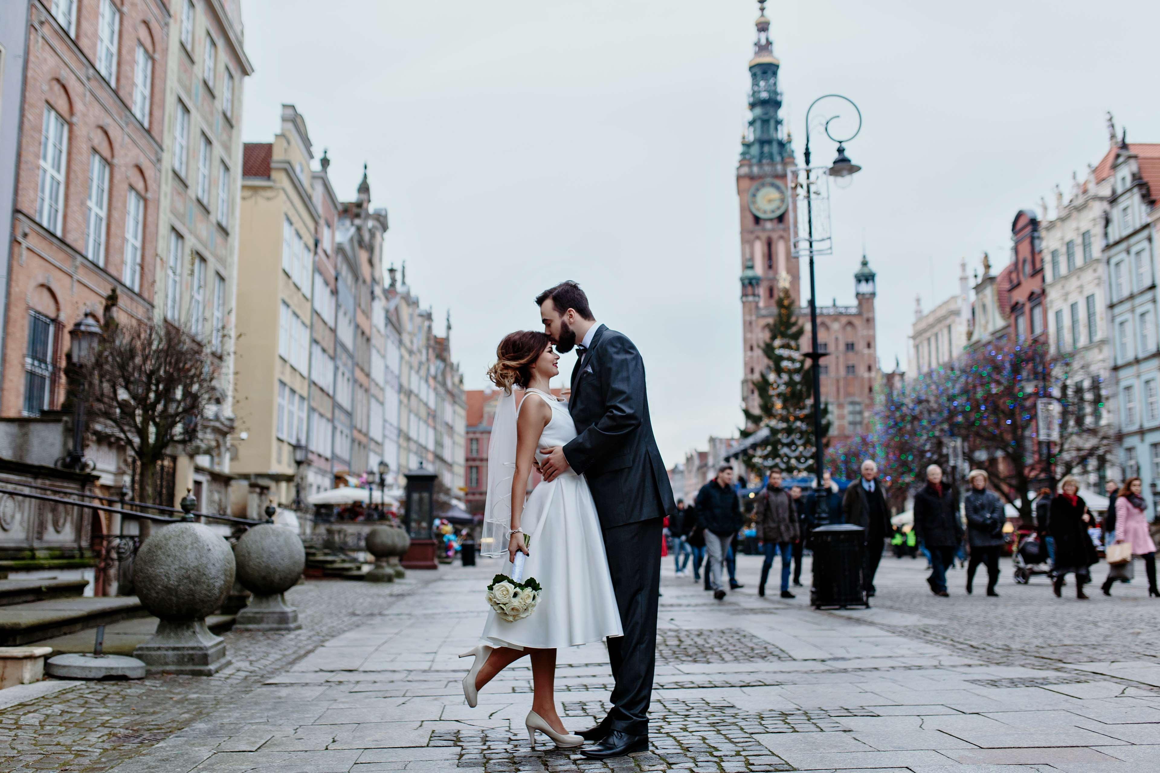 Radisson Blu Hotel, Danzica Esterno foto The photo depicts a joyful moment between a couple in a romantic embrace on a lively street. The woman is wearing a white wedding dress, and the man is dressed in a smart suit. They appear to be celebrating their love, possibly on their wedding day. 