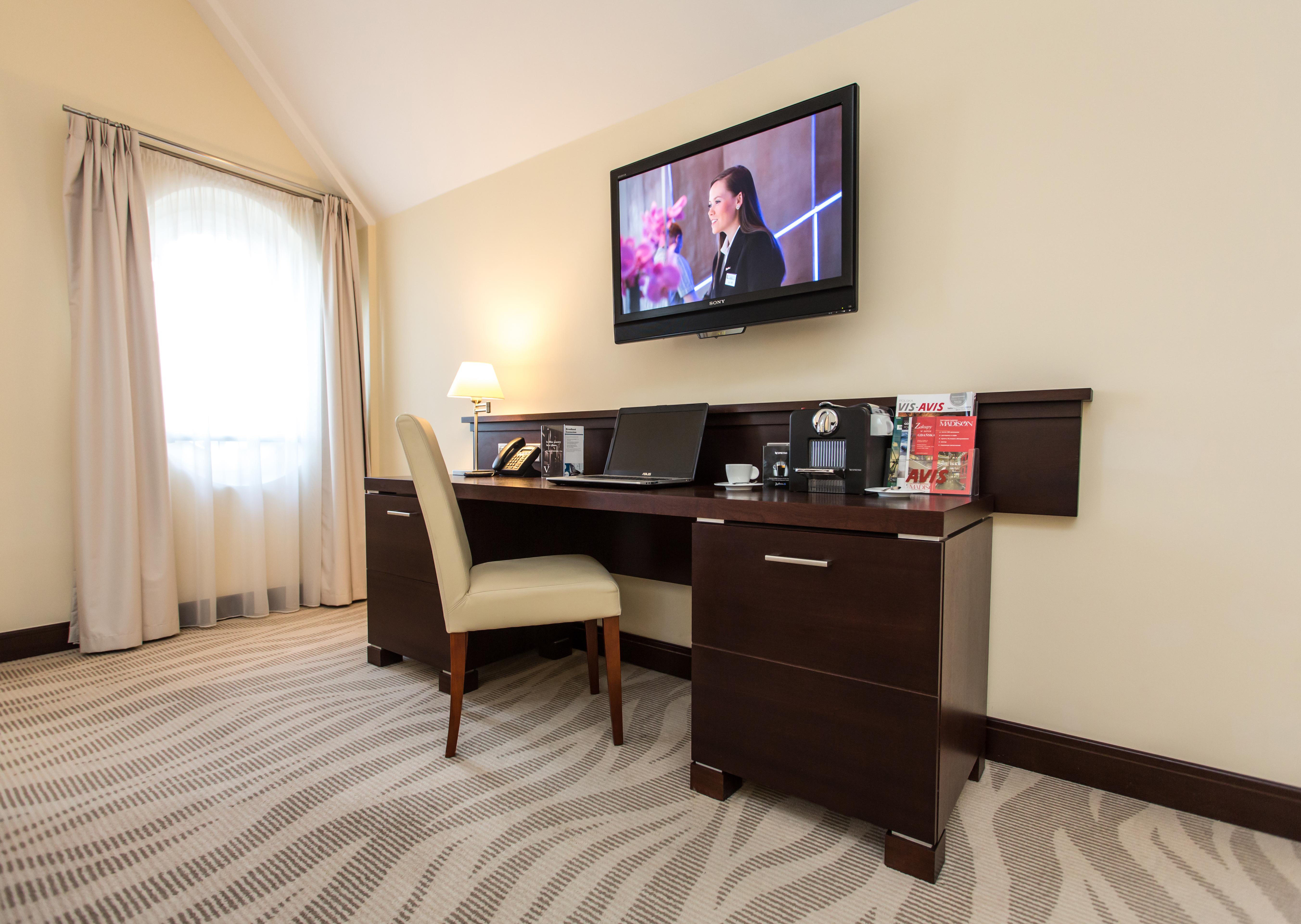 Radisson Blu Hotel, Danzica Esterno foto The photo depicts a corner of a room featuring a stylish desk with a chair and a television mounted on the wall above. The desk has various items on it, possibly including a telephone, clock, and some decorative elements or stationery. There is a lam