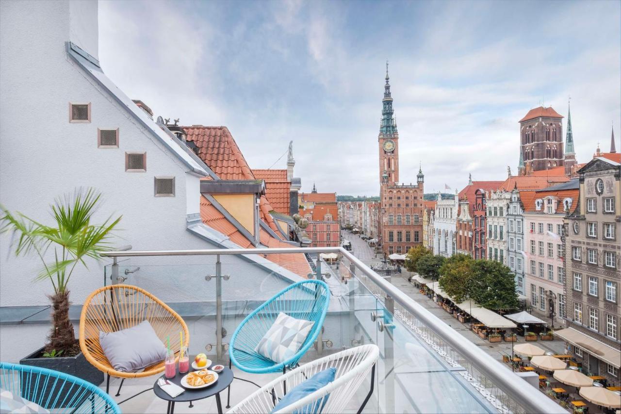 Radisson Blu Hotel, Danzica Esterno foto The photo shows a stylish balcony overlooking a scenic urban landscape. There are two colorful chairs in blue and white, positioned around a small table. On the table, there are desserts and drinks, suggesting a cozy spot for relaxation. In the backg