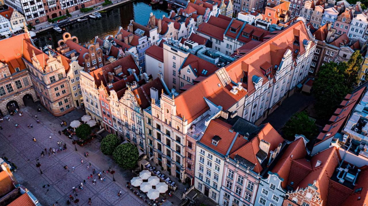 Radisson Blu Hotel, Danzica Esterno foto The photo shows a bird's-eye view of a picturesque urban area, likely in a historical city. It features a cluster of buildings with a mix of architectural styles, characterized by colorful facades and predominantly red rooftops. The buildings seem to