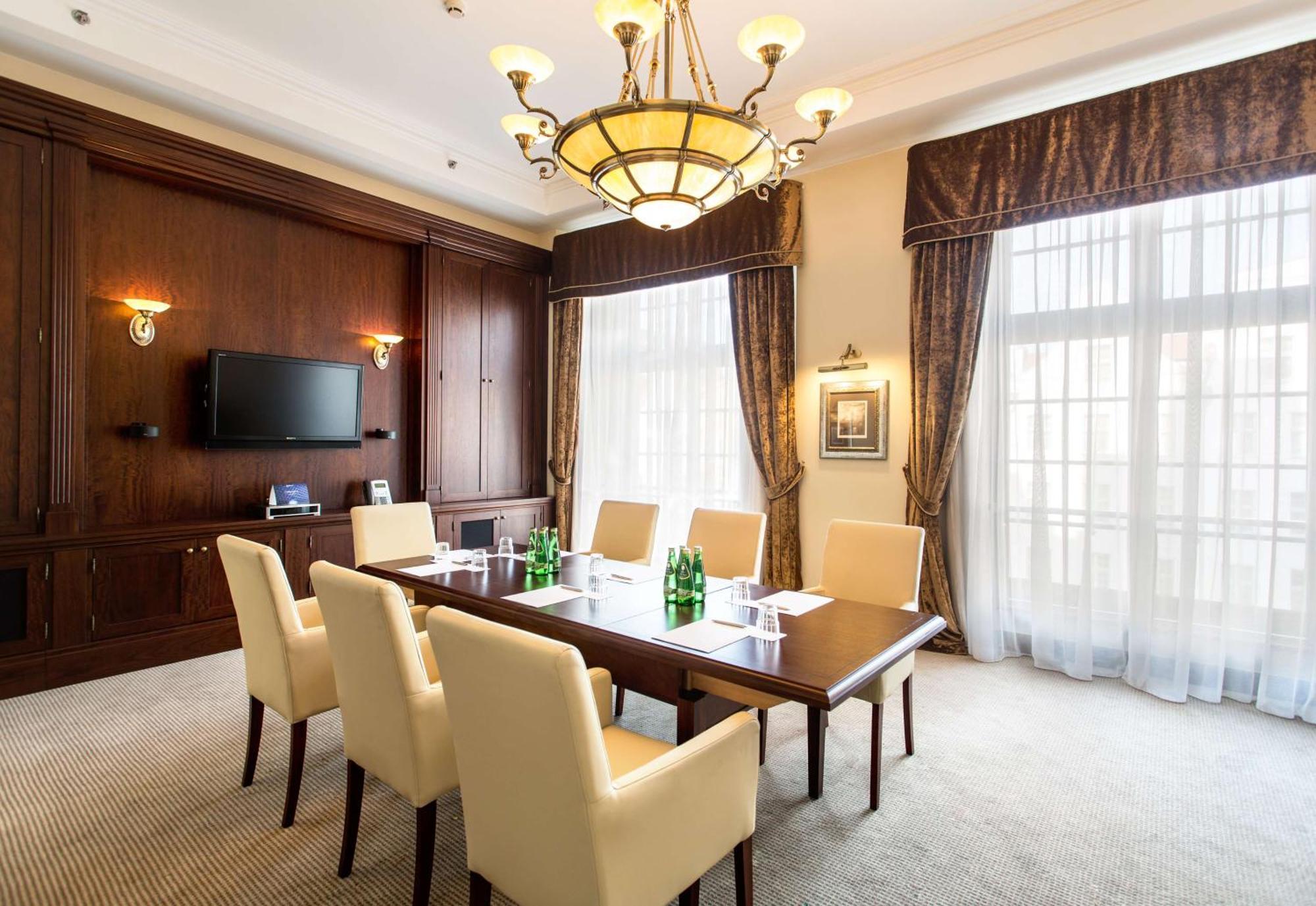 Radisson Blu Hotel, Danzica Esterno foto The photo shows a well-furnished conference room. It features a large wooden table surrounded by six cream-colored chairs. On the table, there are several green glass bottles of water. The room is well-lit with a decorative chandelier hanging from th