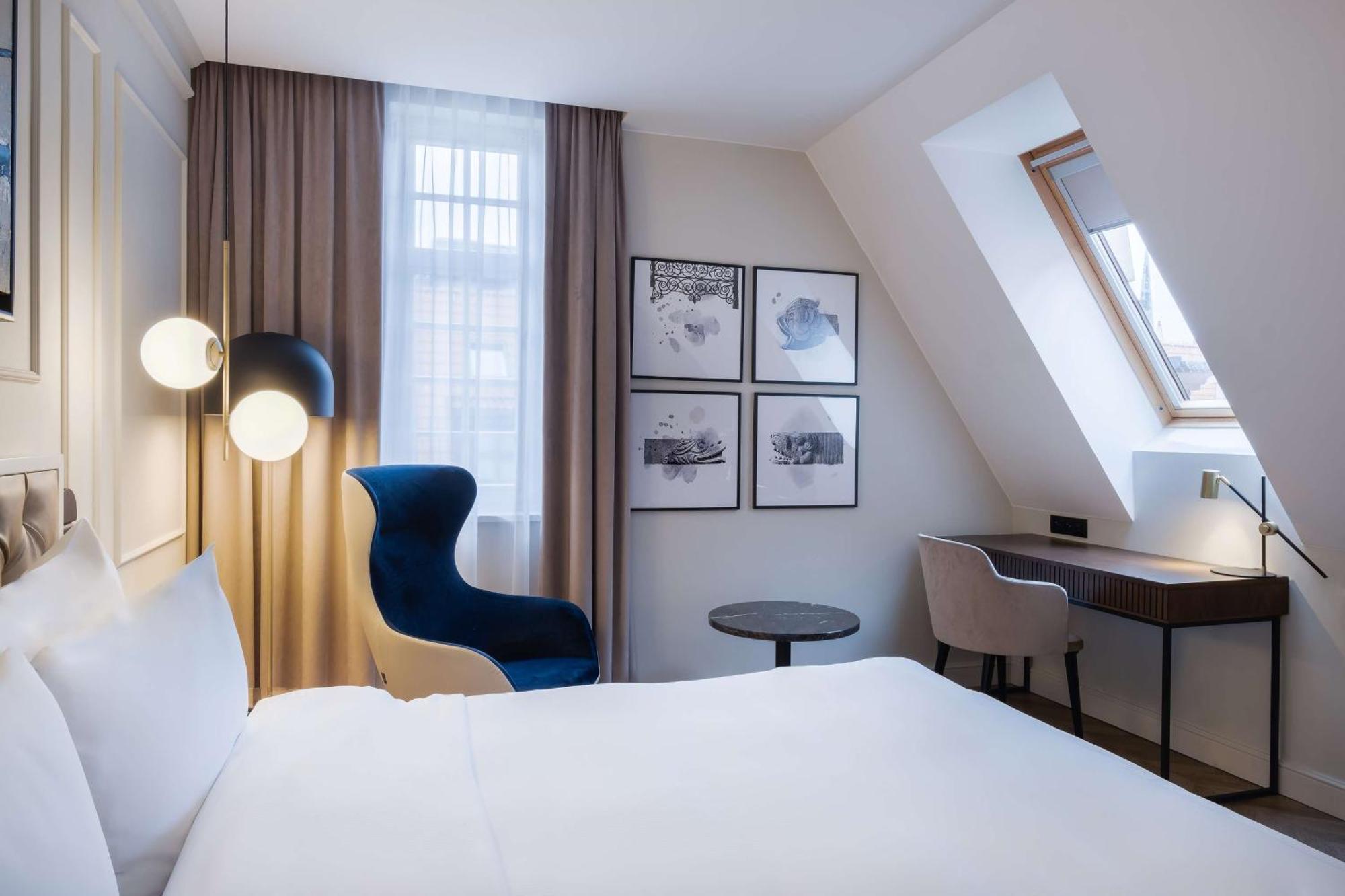 Radisson Blu Hotel, Danzica Esterno foto The photo shows a cozy hotel room featuring a modern design. The room has a double bed with a white duvet, and a large window with sheer curtains that allows natural light to filter in. On the wall opposite the bed, there are several framed artworks.