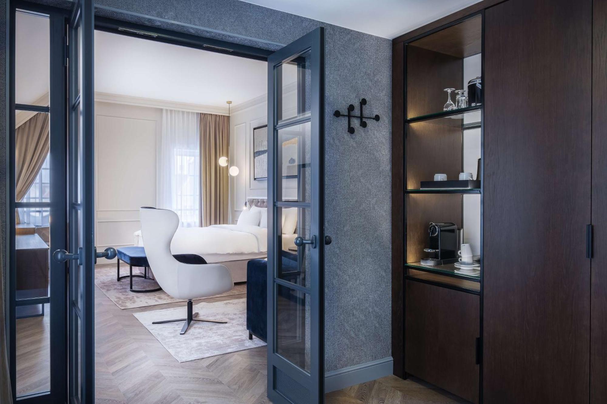 Radisson Blu Hotel, Danzica Esterno foto The photo shows a luxuriously designed hotel room viewed from an entrance. In the foreground, there is a doorway with dark double doors leading into the main area. To the right, there is a wooden cabinet with shelves displaying some items, including 